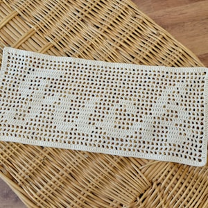 Puede incluir: Tapete rectangular de ganchillo color crema con un delicado patr&oacute;n calado. La pieza hecha a mano se exhibe sobre una superficie de mimbre tejido, mostrando su textura y artesan&iacute;a. Un art&iacute;culo de decoraci&oacute;n para el hogar simple y elegante.