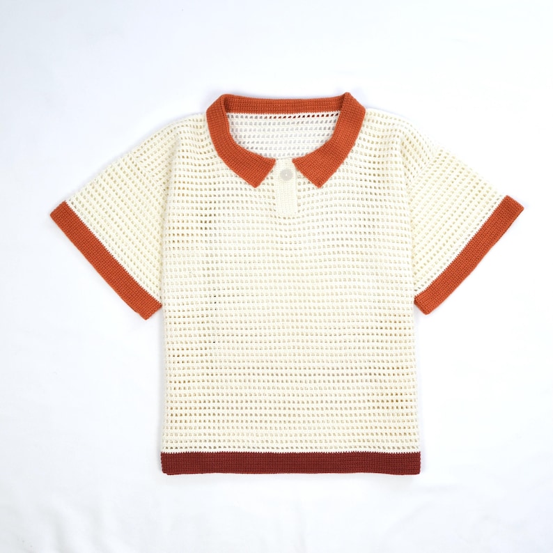 Pode incluir: Camisa polo creme de manga curta com design de croch&ecirc;. A camisa apresenta gola, acabamento das mangas e bainha inferior em laranja queimado. Um &uacute;nico bot&atilde;o branco fecha a gola. A camisa &eacute; exibida em um fundo branco.