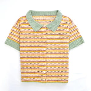 Puede incluir: Una camisa de crochet a rayas con cuello verde y mangas cortas. La camisa tiene un frente abotonado.
