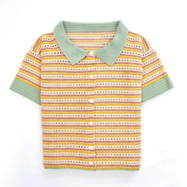 Puede incluir: Una camisa de crochet a rayas con cuello verde y mangas cortas. La camisa tiene un frente abotonado.
