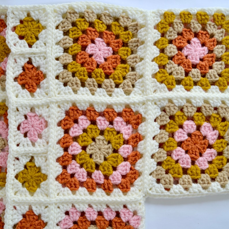 May include: A close-up of a crocheted blanket with a pattern of squares in shades of pink, orange, brown, and yellow.