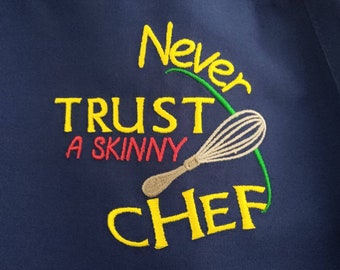 May include: A blue apron with yellow embroidery that reads "Never Trust a Skinny Chef" with a green swirl and a whisk.