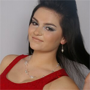 May include: A woman with long black hair wearing a red dress with a crystal necklace and earrings.