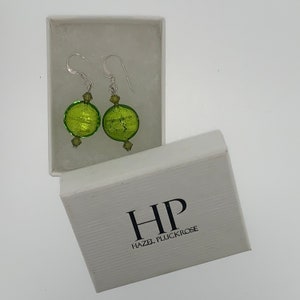 May include: Green glass earrings with silver hooks and a silver bead accent. The earrings are in a white box with the text "HP Hazel Pluckrose".