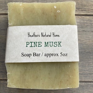 May include: A rectangular bar of soap with a light green hue, wrapped with a white paper band. The band features the text "Heathers Natural Home," "PINE MUSK," and "Soap Bar / approx 5oz."