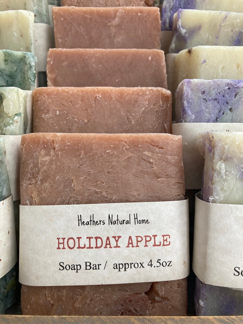 May include: Close-up of several rectangular soap bars in various colors, including shades of brown, green, and purple. One bar is labeled "Holiday Apple" with the text "Soap Bar / approx 4.5oz". The soaps appear to be handmade.