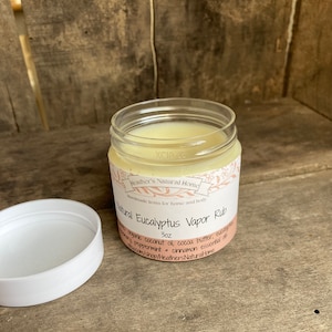 Puede incluir: Un tarro blanco con una tapa transparente que contiene un bálsamo blanco. La etiqueta dice "Heather's Natural Home Handmade Items for Home and Body Natural Eucalyptus Vapor Rub 3oz with organic coconut oil, cocoa butter, eucalyptus, rosemary, peppermint + cinnamon essential oils etsy.com/shop/HeathersNaturalHome"