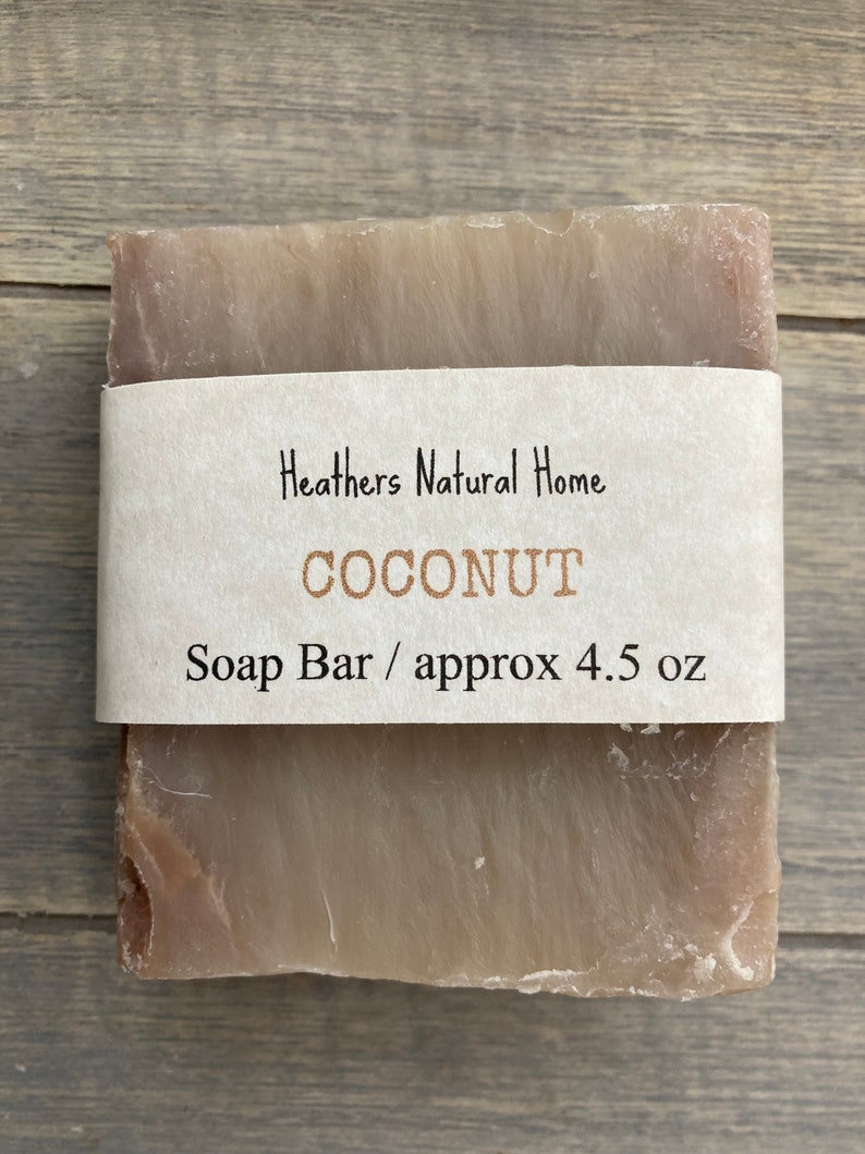 May include: A rectangular bar of soap with a light brown color and a paper label wrapped around it. The label reads "Heathers Natural Home COCONUT Soap Bar / approx 4.5 oz."