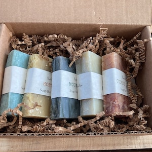 May include: A set of five natural soap bars in a cardboard box with brown paper shred. The soap bars are labeled "Citrus Dream", "Mountain Bloom", "Hope", "Sea Salt", and "Lavender Dream".