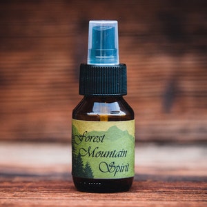 Puede incluir: Una pequeña botella de vidrio marrón con un atomizador negro y una etiqueta verde que dice "Forest Mountain Spirit".