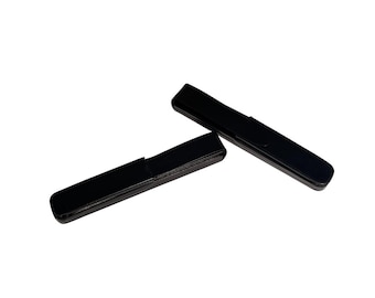 May include: Two black rectangular cases with a hinged lid are displayed against a white background. The cases are sleek and minimalist, with a glossy finish. The cases appear to be empty and are likely designed to hold small items.