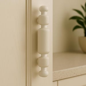 Op de afbeelding: Witte keukendeur met een witte, moderne, cilindrische deurknop. De knop heeft een aantal ronde, gestapelde secties.