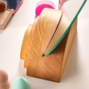 May include: A wooden makeup organizer with a mirror. The organizer has a curved design and is made of light brown wood. The mirror is clear and has a green tint.