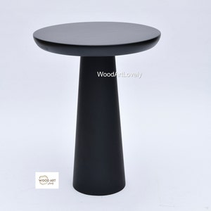 Op de afbeelding: Een zwarte houten bijzettafel met een rond blad en een conische basis. De tafel is gemaakt van massief hout en heeft een gladde afwerking. De tafel is ongeveer 50 cm hoog en 40 cm in diameter.