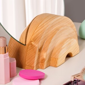 May include: A wooden rainbow-shaped stand with a round mirror on top. The stand is made of light wood and has a natural finish. The mirror is clear and has a silver frame.