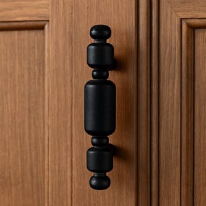 Puede incluir: Pomo de armario negro con un diseño geométrico redondeado. El pomo está hecho de madera y tiene un acabado mate.