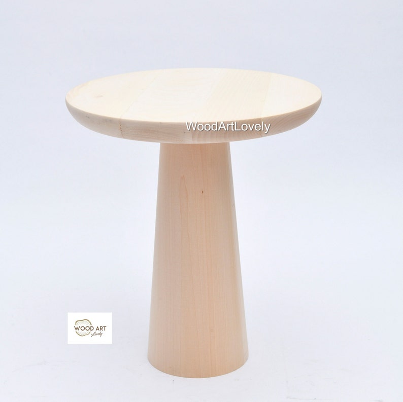Op de afbeelding: Een licht houten bijzettafel met een rond blad en een hoge, cilindrische basis. De tafel is gemaakt van natuurlijk hout en heeft een eenvoudig, modern ontwerp. De tekst "WoodArtLovely" is zichtbaar op het tafelblad.