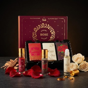 May include: A rose-themed attar set with a burgundy box and gold accents. The set includes several small perfume bottles, rose petals, and a few white roses. The text on the box reads "ATTAR SET ROSE".