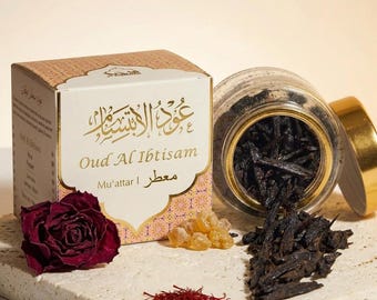 Pode incluir: Uma caixa de produto com escrita árabe dourada e as palavras em inglês "Oud Al Ibtisam". Um frasco de vidro com tampa dourada está aberto, revelando lascas de madeira escura. Uma rosa vermelha seca, açafrão e resina de cor âmbar também estão presentes.