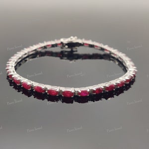 May include: A silver bracelet featuring a series of oval-cut, vibrant red gemstones. The gemstones are set closely together, creating a continuous line of color. The bracelet is designed with a secure clasp.