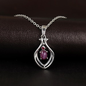 Pode incluir: Um colar de prata com um delicado pingente de design vazado que apresenta uma gema rosa. O pingente tem a forma de uma lágrima e tem uma pequena gema rosa na parte superior.