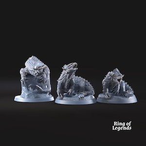May include: Three light blue fantasy figurines of reptilian creatures. One is perched on a rock, another is seated with its mouth open, and the third is crouched. The figurines are on circular bases.