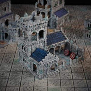 Peut inclure: Un bâtiment en pierre grise avec une tour et un toit bleu. Le bâtiment possède une petite cour avec deux cibles rouges et blanches. Le bâtiment est fait d'un matériau texturé et a un aspect réaliste.