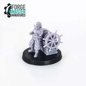 Puede incluir: Una miniatura de plástico gris de una figura barbuda de pie junto a una rueda de barco. La figura lleva un abrigo largo y sostiene una daga. La miniatura está sobre una base negra.