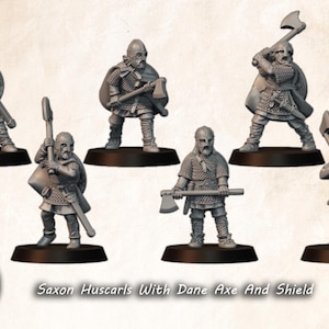 May include: A collection of grey miniature Saxon Huscarl figures, each holding a Dane axe and shield. The figures are on black bases, with detailed chainmail and helmets. The text "Saxon Huscarls With Dane Axe And Shield" is displayed below the figures.