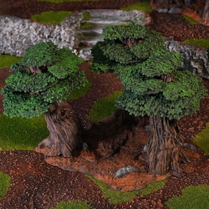 Puede incluir: Dos árboles en miniatura con troncos marrones texturizados y follaje verde vibrante. Los árboles están sobre una base marrón, rodeados de terreno verde y marrón, lo que sugiere un paisaje en miniatura o un diorama. La escena evoca un entorno natural al aire libre.