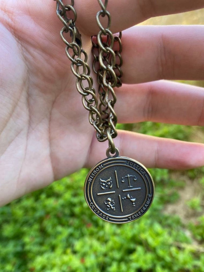 May include: A gold-toned necklace with a round pendant featuring four symbols: an owl, a scale, a lion, and a chalice. The pendant is inscribed with the words "Wisdom", "Justice", "Courage", and "Temperance".
