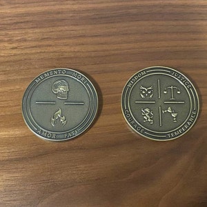 May include: Two gold-colored metal coins with engraved designs. The first coin features a skull and flames with the words "Memento Mori", "Amor", and "Fati". The second coin features a series of symbols and the words "Wisdom", "Justice", "Courage", and "Temperance".