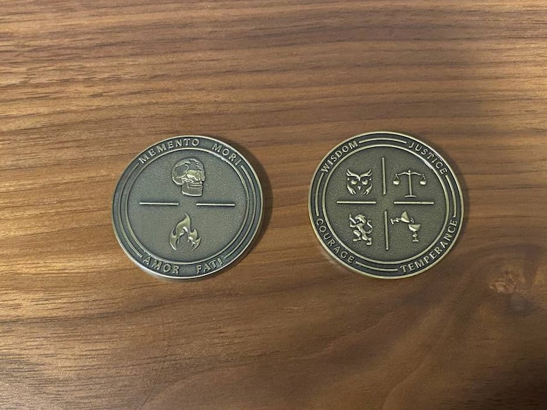 May include: Two gold-colored metal coins with engraved designs. The first coin features a skull and flames with the words "Memento Mori", "Amor", and "Fati". The second coin features a series of symbols and the words "Wisdom", "Justice", "Courage", and "Temperance".