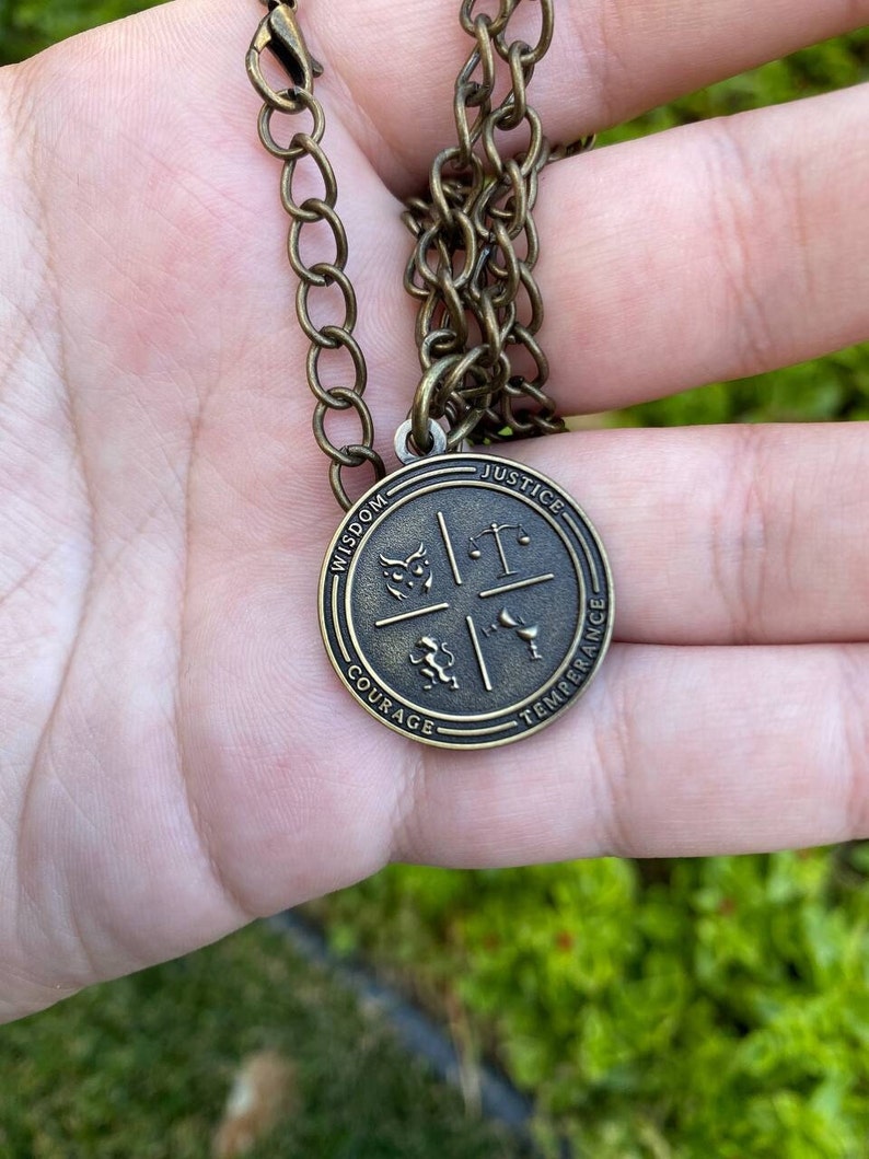 May include: A gold-toned necklace with a round pendant featuring four symbols representing wisdom, justice, courage, and temperance. The pendant is inscribed with the words "Wisdom", "Justice", "Courage", and "Temperance".