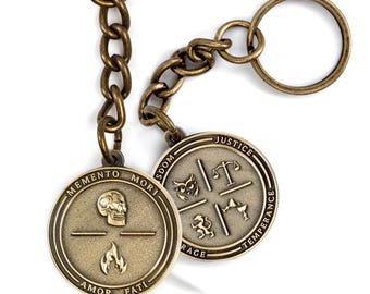 May include: Two antique brass-toned metal keychains featuring circular medallions. One medallion displays a skull, flame, and the text MEMENTO MORI AMOR FATI. The other shows an owl, scales, lion, and chalice with the words WISDOM, JUSTICE, TEMPERANCE, COURAGE.
