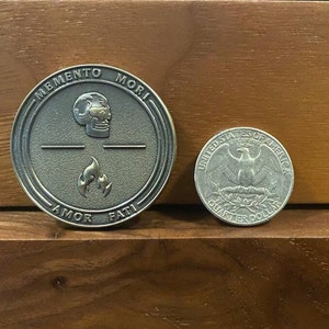 May include: A bronze coin with the words "Memento Mori" and "Amor Fati" inscribed around the edge. The coin features a skull and flames in the center.