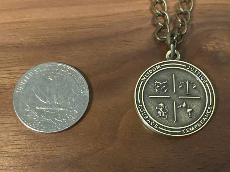May include: A gold-toned pendant necklace with a round charm featuring four symbols and the words "Wisdom", "Justice", "Courage", and "Temperance".