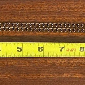 May include: A gold chain necklace with a round pendant featuring a design. The chain is measured with a tape measure, showing a length of 12 inches.