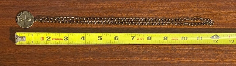 May include: A gold chain necklace with a round pendant featuring a design. The chain is measured with a tape measure, showing a length of 12 inches.
