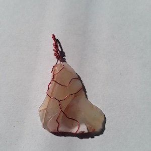 May include: A pendant made from a piece of agate with a natural pattern of white and pink. The agate is wrapped with red wire.