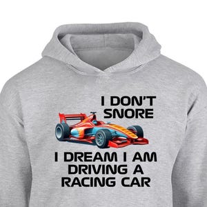 Może przedstawiać: Jasnoszara bluza z kapturem z napisem "I DON'T SNORE I DREAM I AM DRIVING A RACING CAR". Poniżej tekstu znajduje się kolorowa ilustracja samochodu wyścigowego. Samochód wyścigowy jest czerwony, pomarańczowy i niebieski.