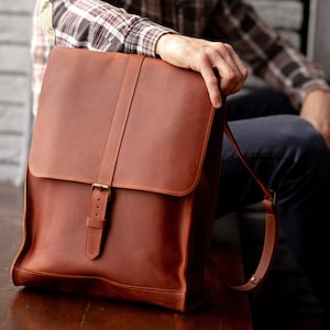 Könnte beinhalten: Ein brauner Lederrucksack mit einer Schnallenverschluss und verstellbaren Trägern. Der Rucksack ist aus hochwertigem Leder gefertigt und hat ein klassisches Design.