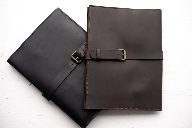 May include: Two leather folders with straps and buckles. The folder on the left is black and the folder on the right is brown.