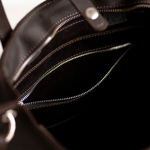 May include: The inside of a brown leather tote bag with a zippered pocket. The bag has a zipper closure and a top handle.