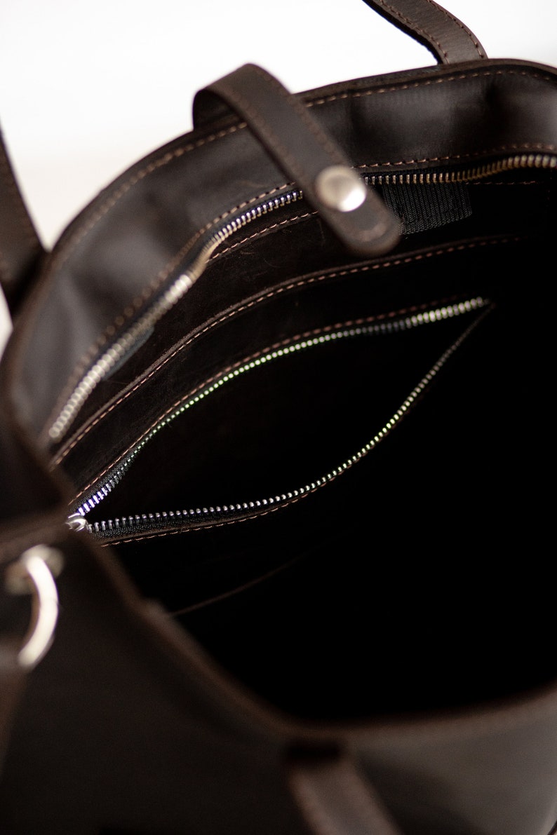 May include: The inside of a brown leather tote bag with a zippered pocket. The bag has a zipper closure and a top handle.