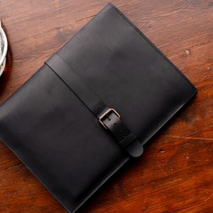 May include: A black leather laptop sleeve with a buckle closure.