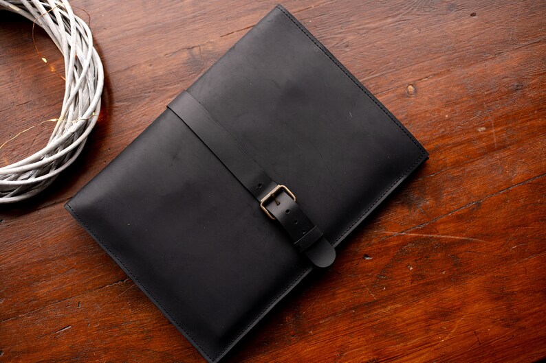 May include: A black leather laptop sleeve with a buckle closure.
