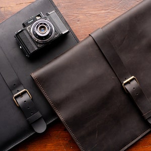 May include: Two leather camera bags with buckles. One bag is black and the other is brown.