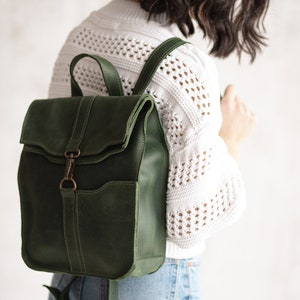 May include: A dark green leather backpack with a flap closure and a front pocket. The backpack has adjustable straps and a metal buckle.