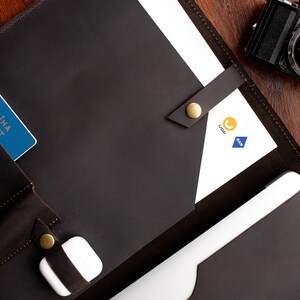 May include: A brown leather portfolio with a passport, a white phone charger, and a white sheet of paper with the logos "Ukr" and "KAA" printed on it.